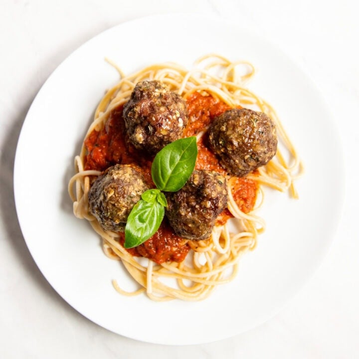 Looking down at a plate of spaghetti and meatballs topped with a fresh basil leaf garnish.