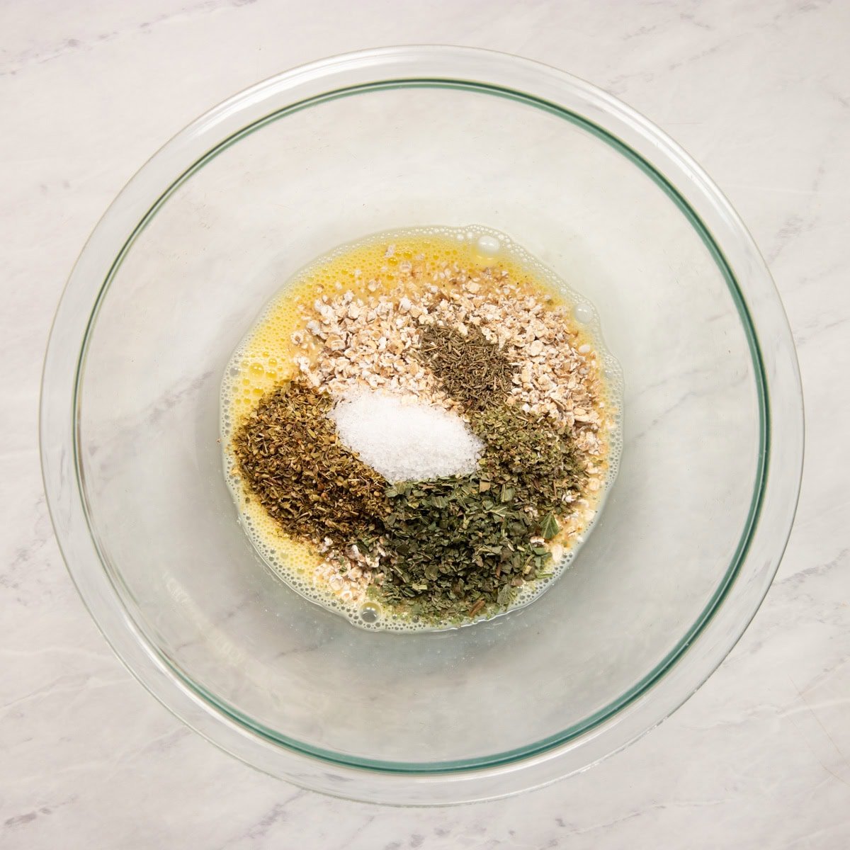 A large mixing bowl containing whisked egg, low FODMAP milk, quick oats and Italian herbs.