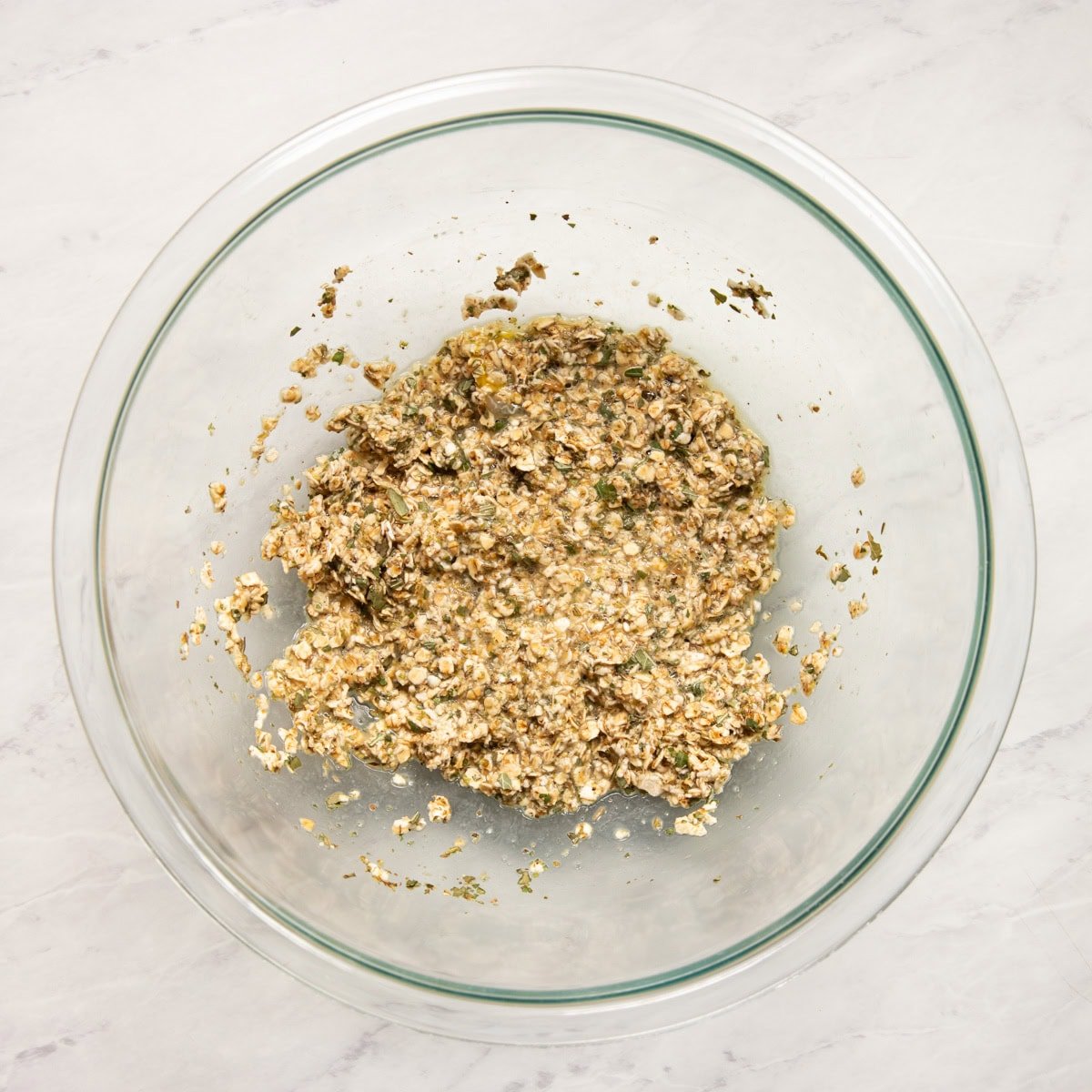 Quick oats and dried Italian herbs have soaked up egg and low FODMAP milk in a large glass mixing bowl. 