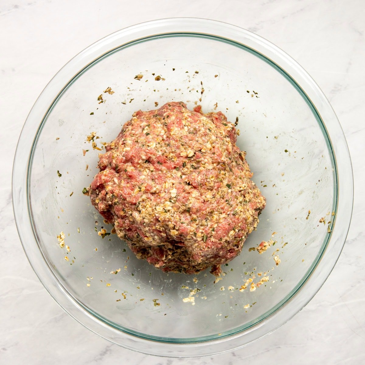 Ground beef is mixed with soaked oats and Italian herbs and is ready to roll into meatballs.