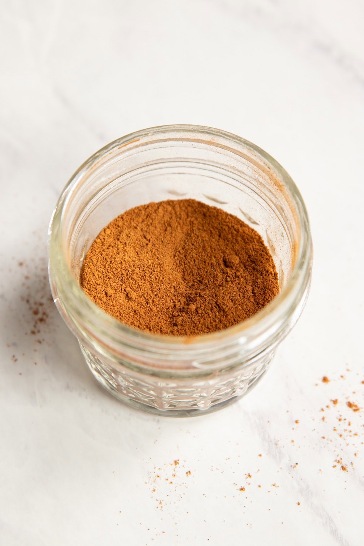 A jar of low FODMAP pumpkin pie spice sits on a white marble counter.