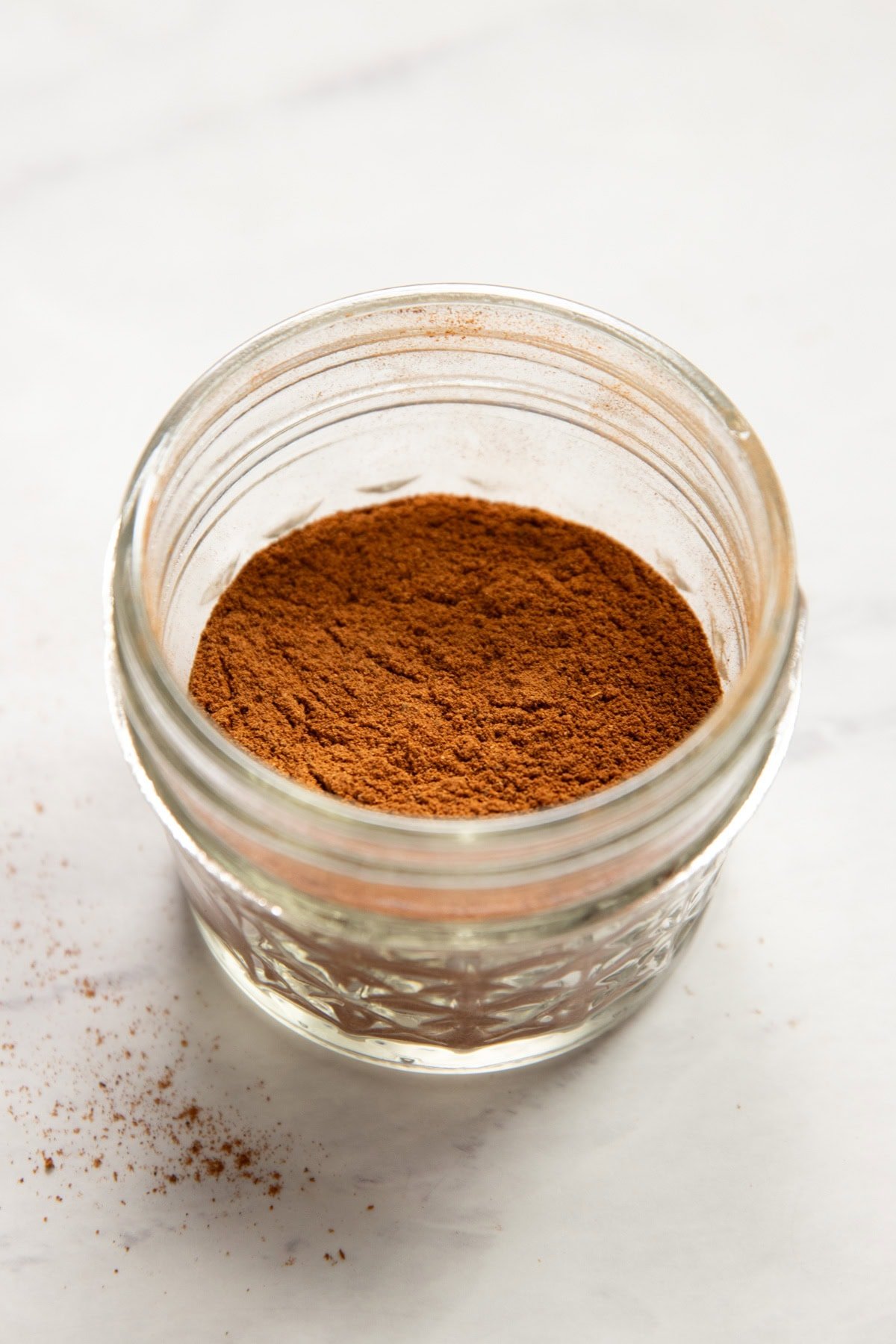 A jar of homemade pumpkin pie spice sits on a white counter.