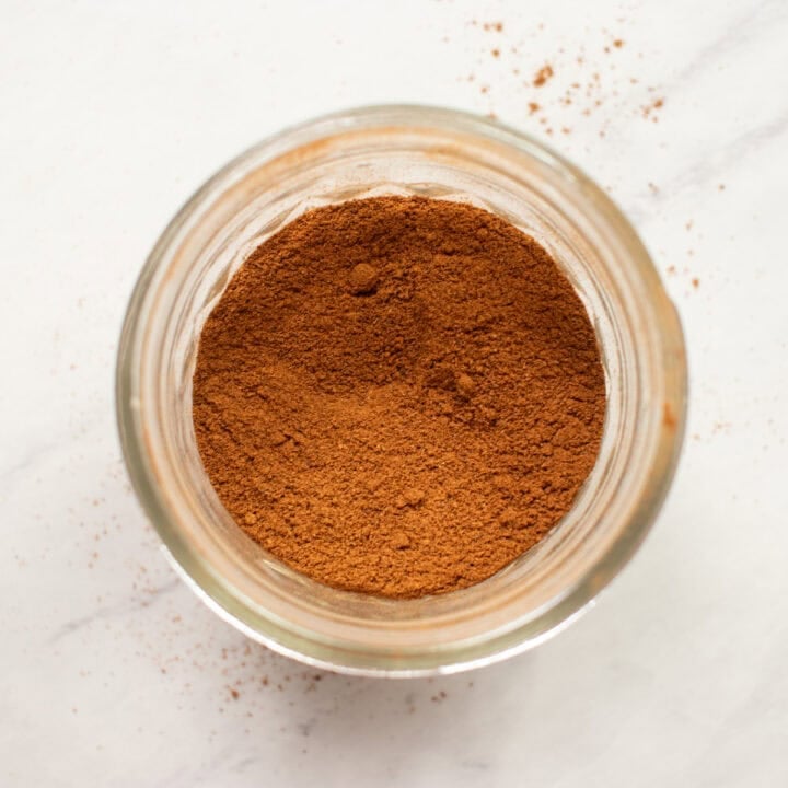 Looking down into small glass jar filled with homemade pumpkin pie spice. Extra is artistically "spilled" around the jar on the counter.