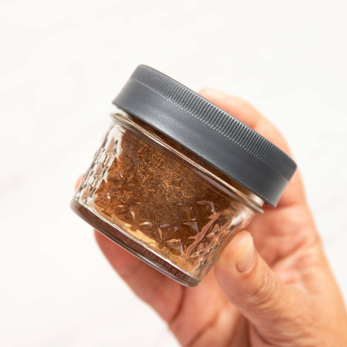 A hand is shaking a sealed mason jar containing homemade pumpkin pie spice.