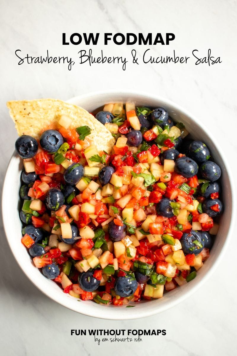 A bowl of fruit salsa with a corn tortilla chip dipped into it.  In the white space above, black text reads "Low FODMAP Strawberry, Blueberry, and Cucumber Salsa."