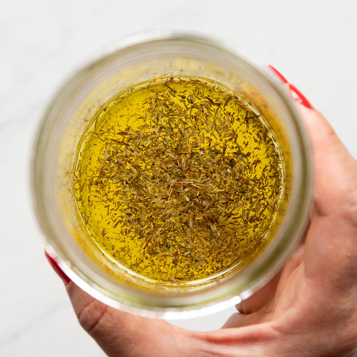 A hand holding a mason jar filled with a lemon-thyme dressing.