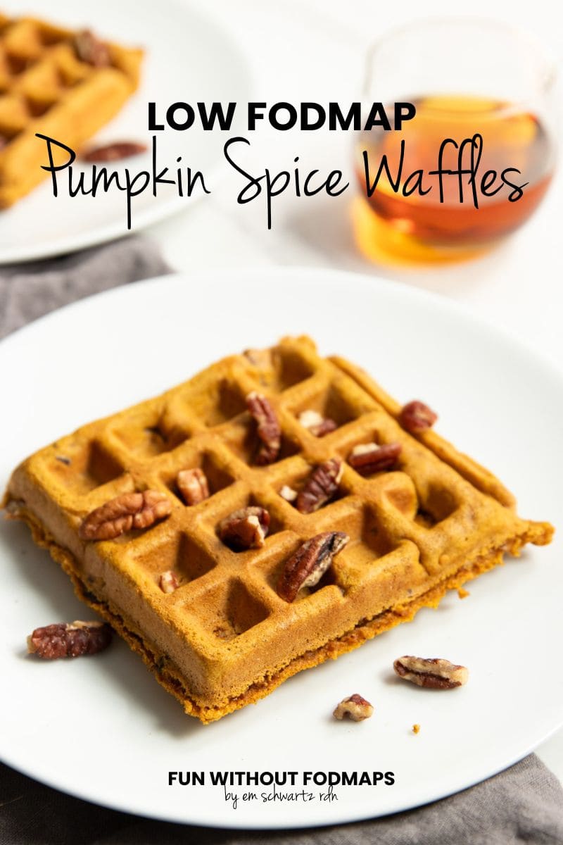 A waffle topped with chopped pecans and maple syrup sits on a plate. There's a small glass pitcher of maple syrup and another plate with a waffle in the background. In the white space above, black text reads "Low FODMAP Pumpkin Spice Waffles."