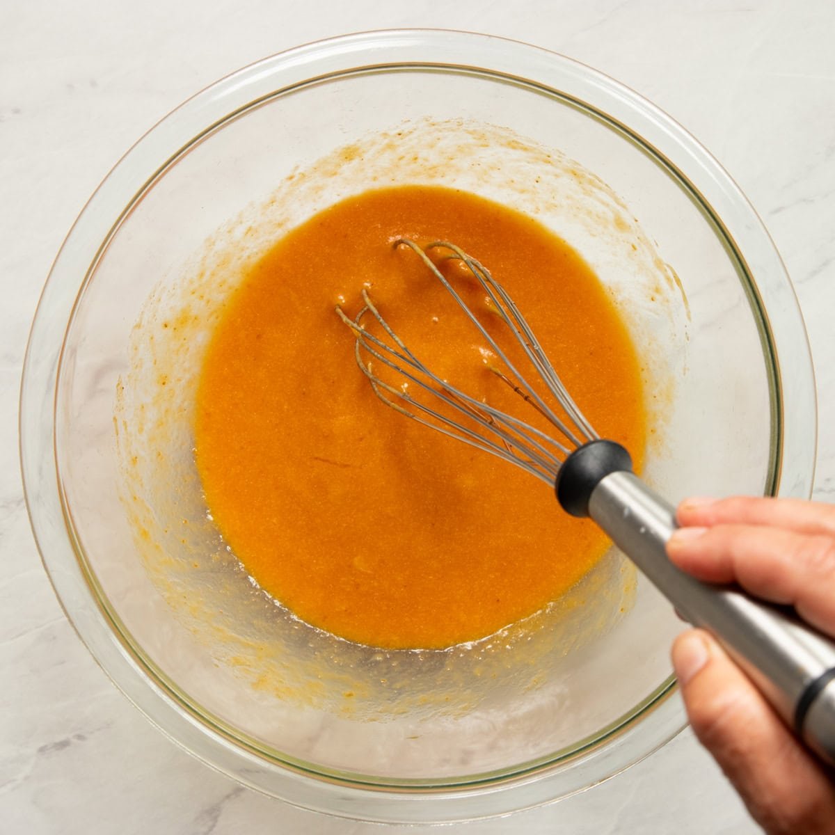 Wet ingredients for pumpkin waffles whisked in a large glass bowl. 
