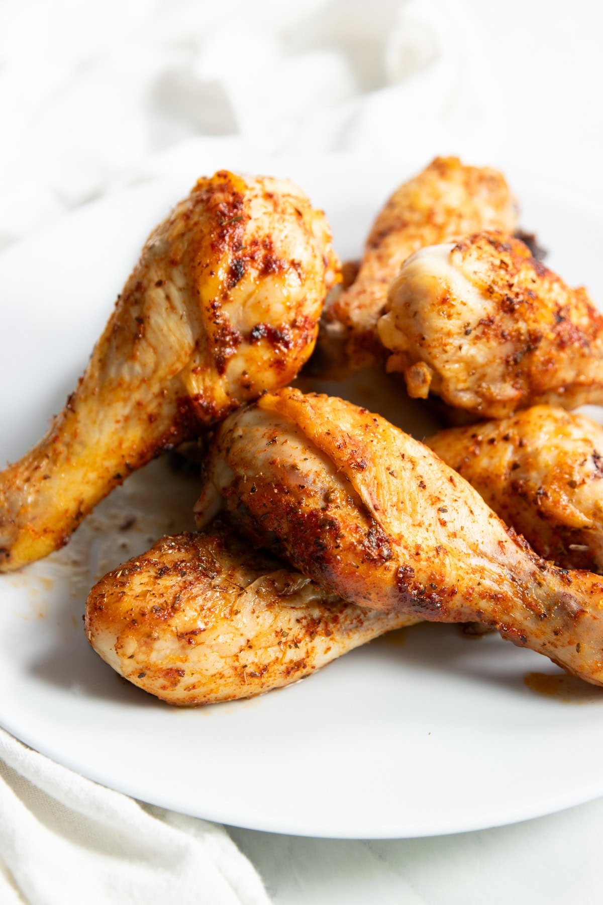 A pile of low FODMAP baked chicken drumsticks on a smooth white plate. A white cotton napkin surrounds the plate's left side.