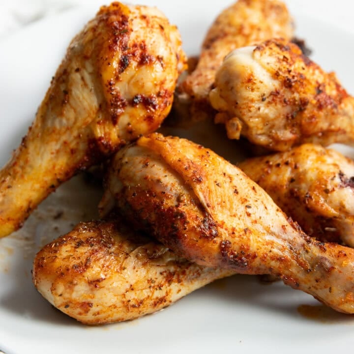 A pile of golden brown low FODMAP baked chicken drumsticks on a smooth white plate.