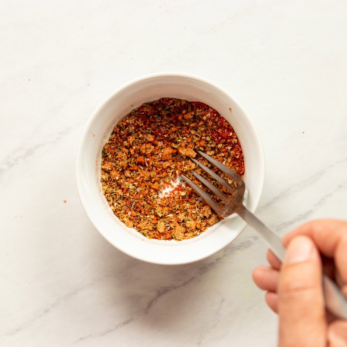 Stirring a spice blend in a small bowl with a fork.