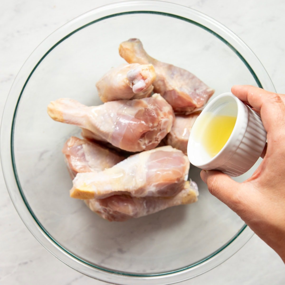 Drizzling avocado oil over a chicken drumsticks in a large mixing bowl.