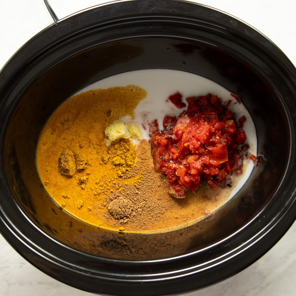 Ingredients needed to make curry base are put in the bottom of a slow cooker.