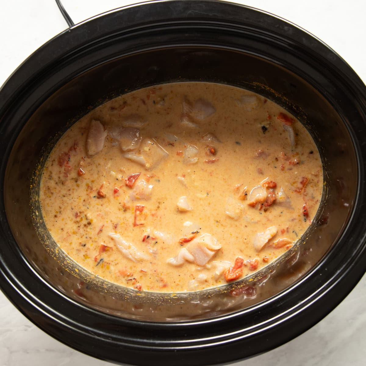 The curry base is mixed and cubed chicken is added to a slow cooker.