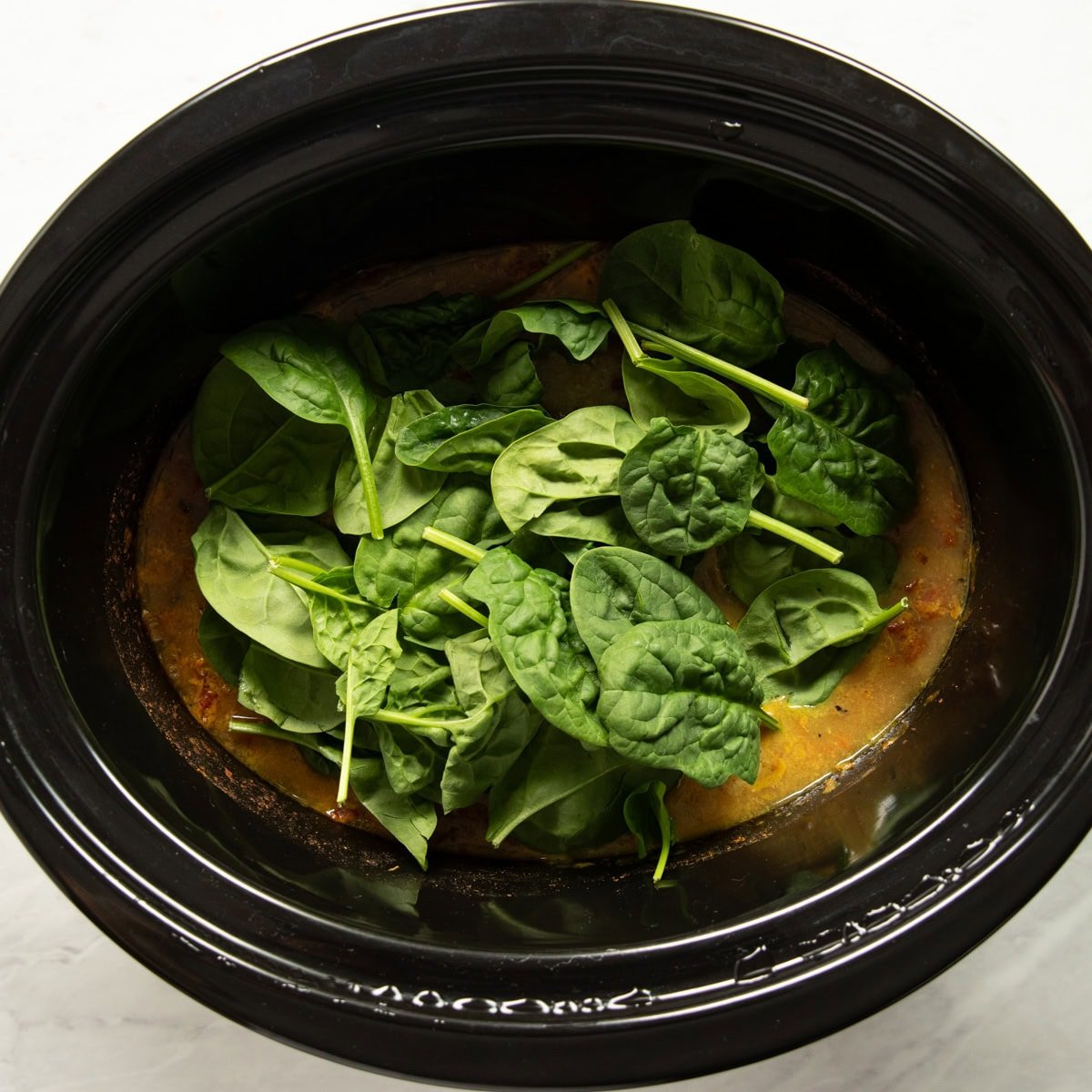 Baby spinach is added on top of the cooked curry ready to be stirred in and wilted.