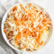 Looking down at a big bowl of Low FODMAP Vinegar Coleslaw sitting on white marble counter with a white cotton napkin off on the side.