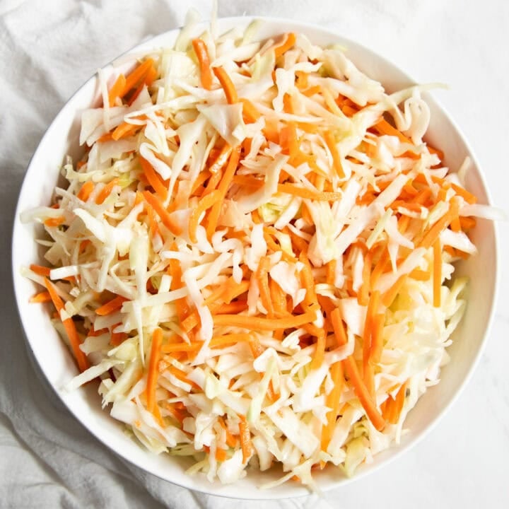 Looking down at a big bowl of Low FODMAP Vinegar Coleslaw sitting on white marble counter with a white cotton napkin off on the side.