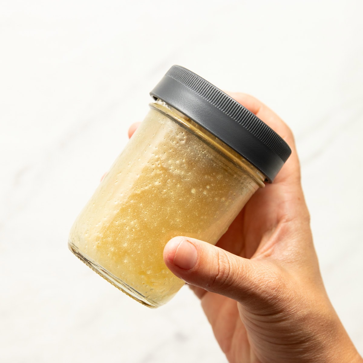 Shaking vinegar coleslaw dressing in a sealed mason jar.
