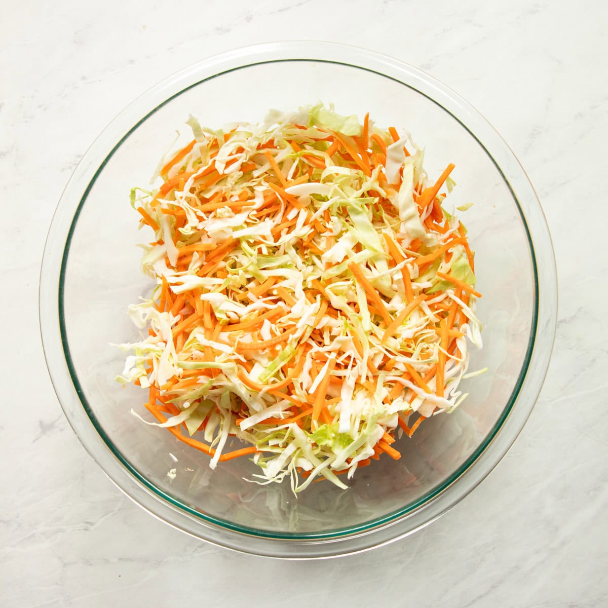 Shredded cabbage and carrots are mixed in a large glass bowl.
