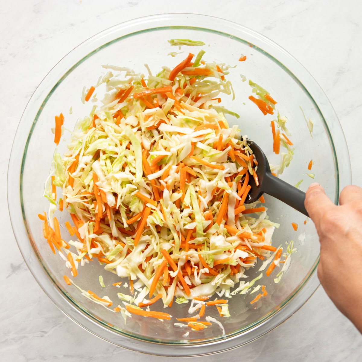 Vinegar dressing is being mixed with shredded cabbage and carrots.