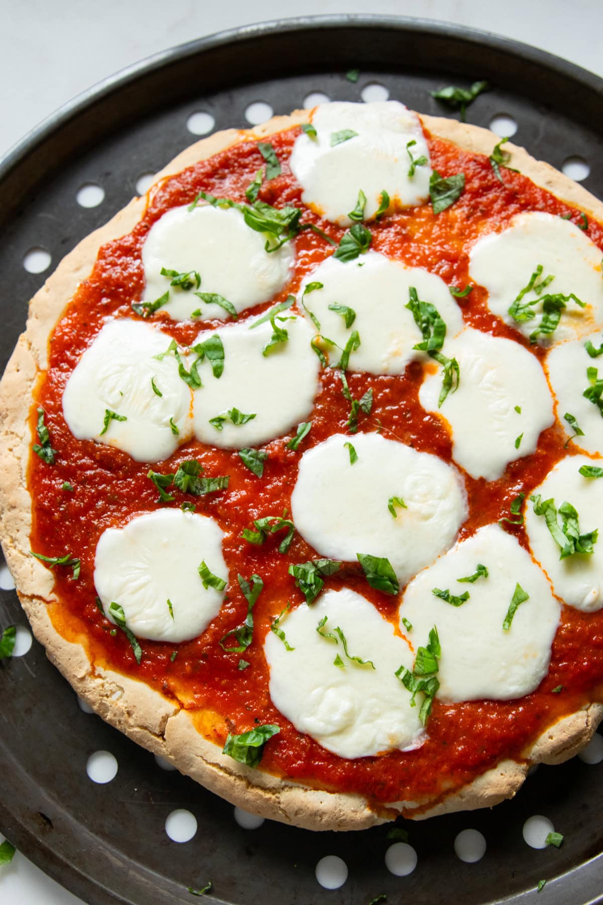 A baked gluten-free and low FODMAP pizza topped with melted fresh mozzarella and fresh basil.