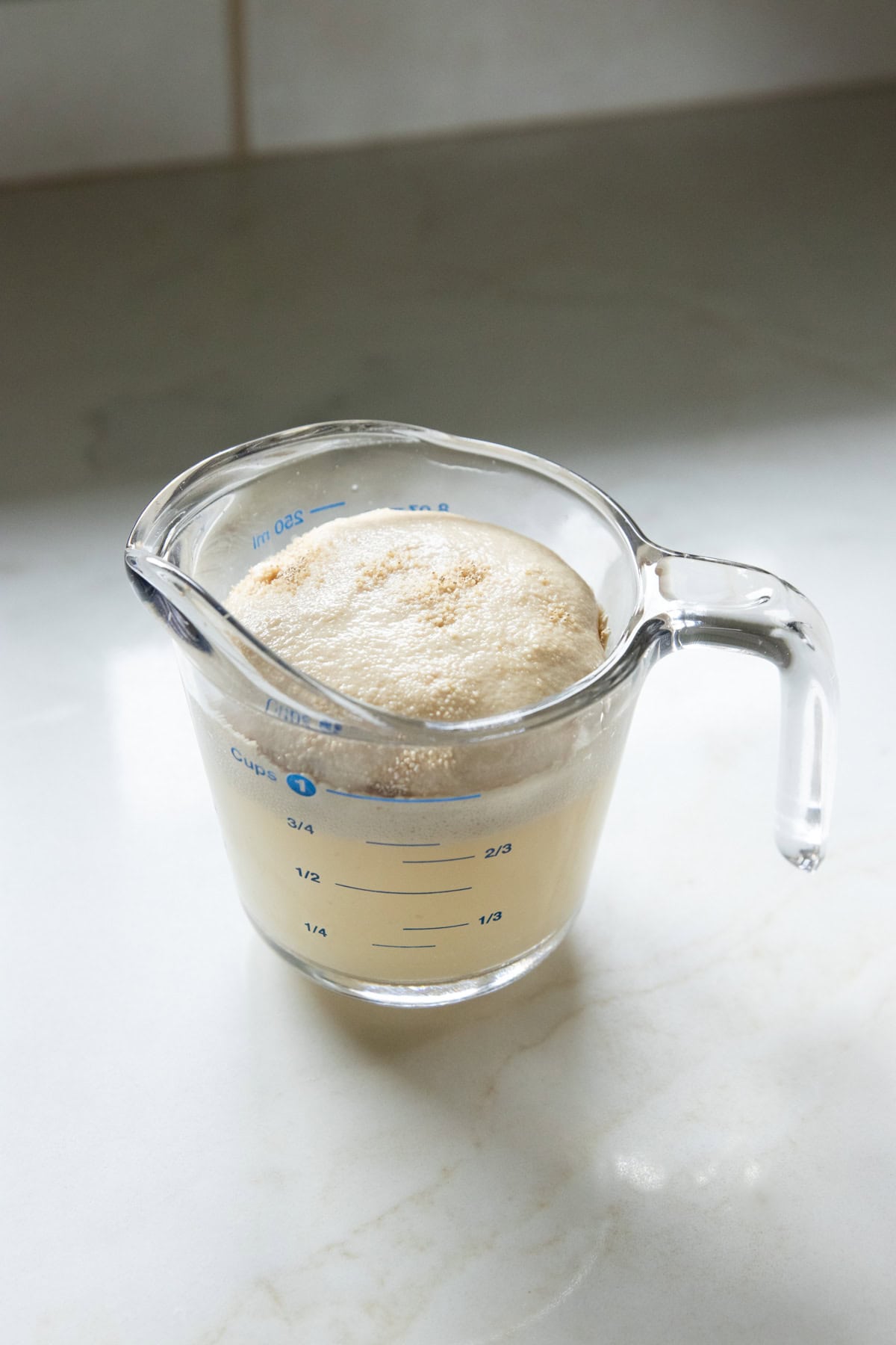 Foamy yeast mixture in a glass measuring cup used to activate yeast for gluten-free pizza dough.