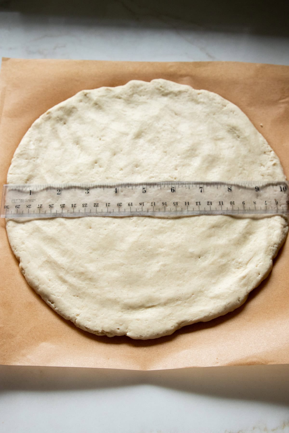Gluten-free pizza dough hand-pressed into a 10-inch round. A clear ruler lays on top to confirm diameter.