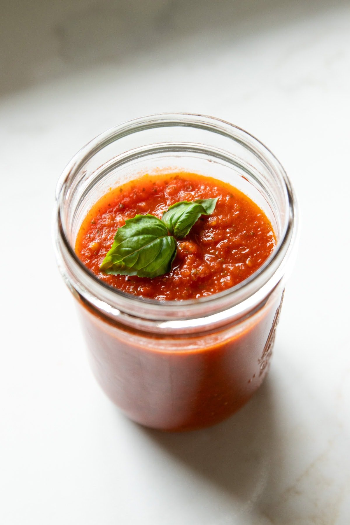 A mason jar filled with homemade pizza sauce sits on a white countertop.