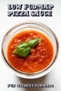 Looking into a glass jar filled with tomato sauce topped with fresh basil leaves. In the white space, black text reads Low FODMAP Pizza Sauce.