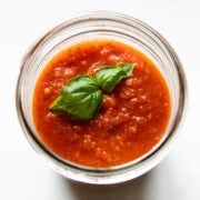 Looking into a mason jar filled with Low FODMAP Pizza Sauce. Two basil leaves rest on top of the sauce.