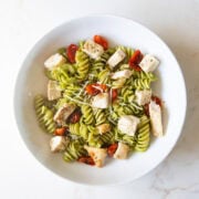 A shallow bowl filled with pesto-covered fusilli pasta, roasted tomatoes, and diced chicken.