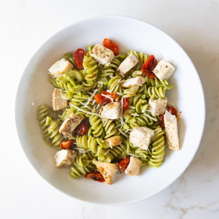 A shallow bowl filled with pesto-covered fusilli pasta, roasted tomatoes, and diced chicken.