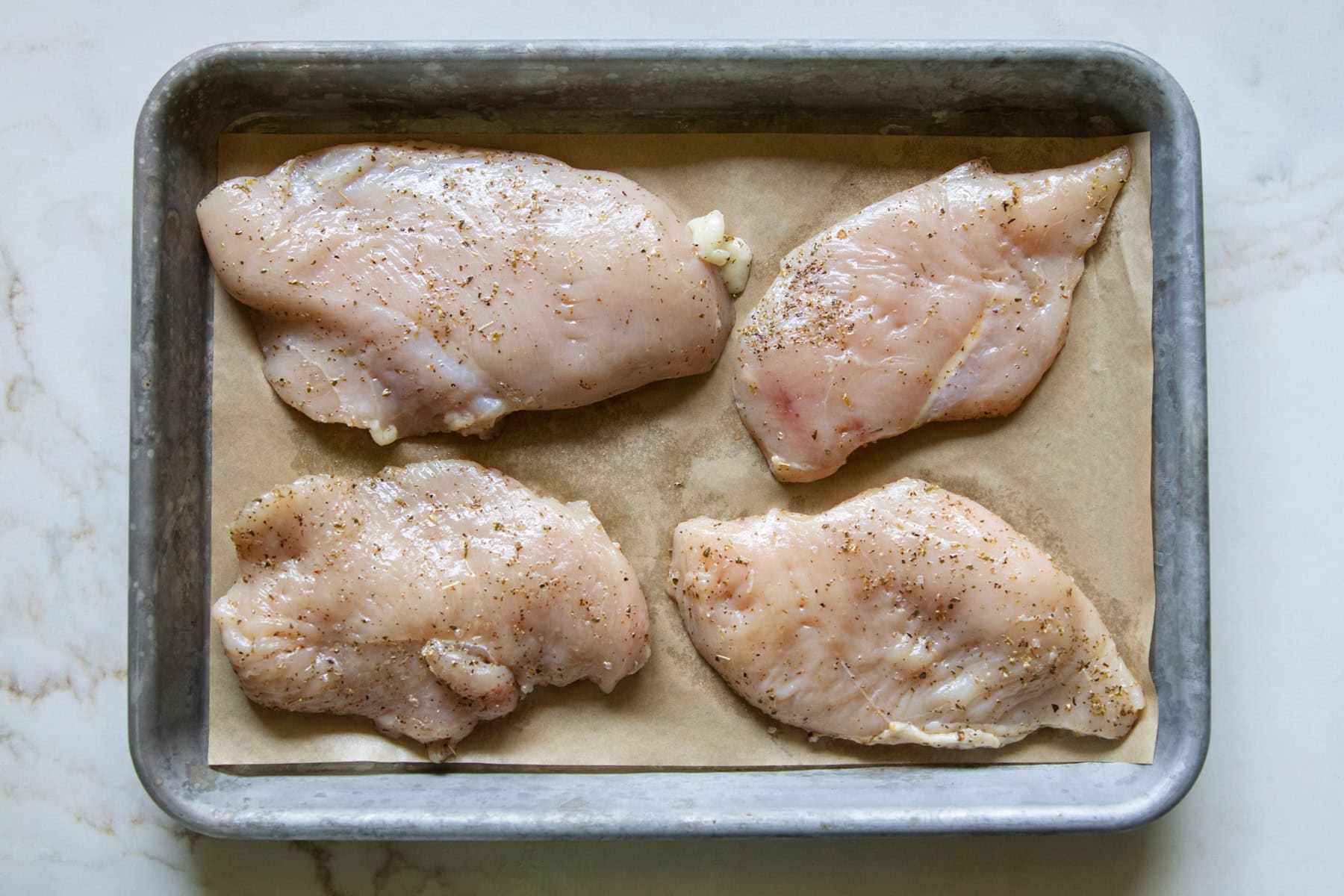 Four thin chicken breasts rubbed in olive oil and dried oregano and placed on a parchment lined sheet pan.