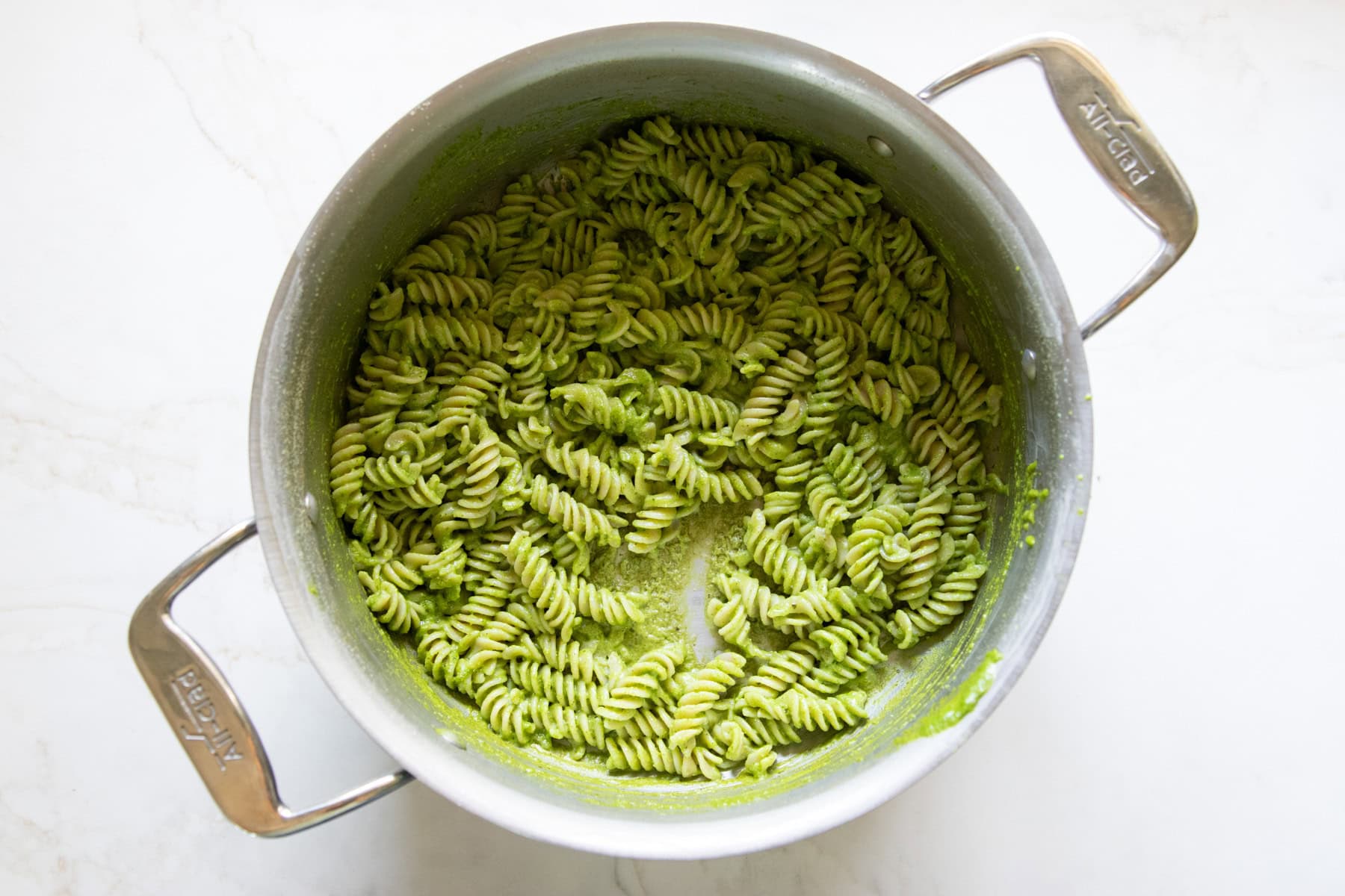 Cooked brown rice fusilli is mixed with low FODMAP pesto in a large pot.