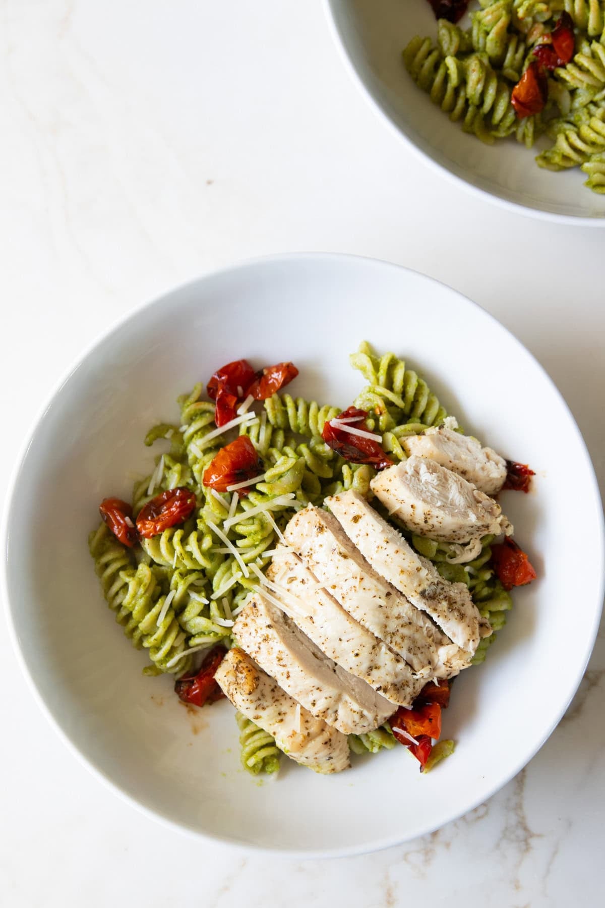 Two shallow bowls filled with low FODMAP pesto pasta with roasted chicken and tomatoes