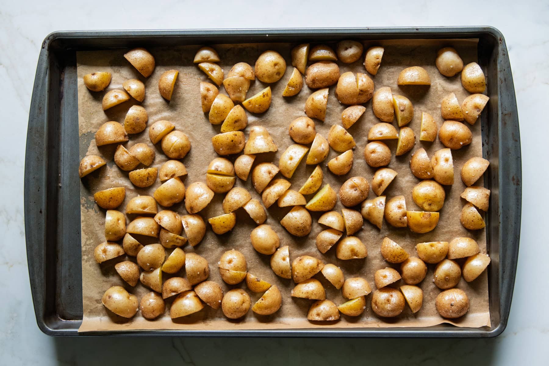 Sheet pan filled with halved and quartered baby yellow potatoes ready for baking.