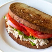 Two slices of toasted gluten-free bread sandwich a low FODMAP tuna salad filling layered with lettuce and tomato.